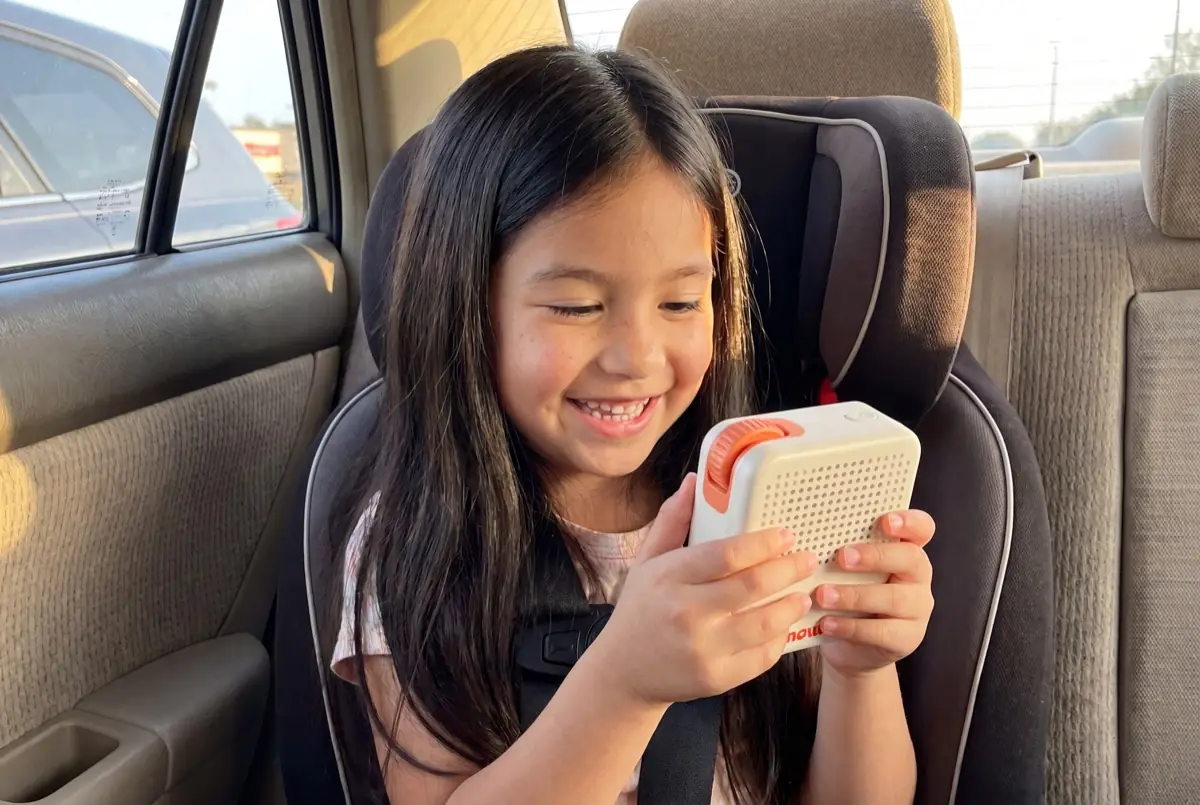 A smiling girl in a car seat holding her Nowa device with both hands